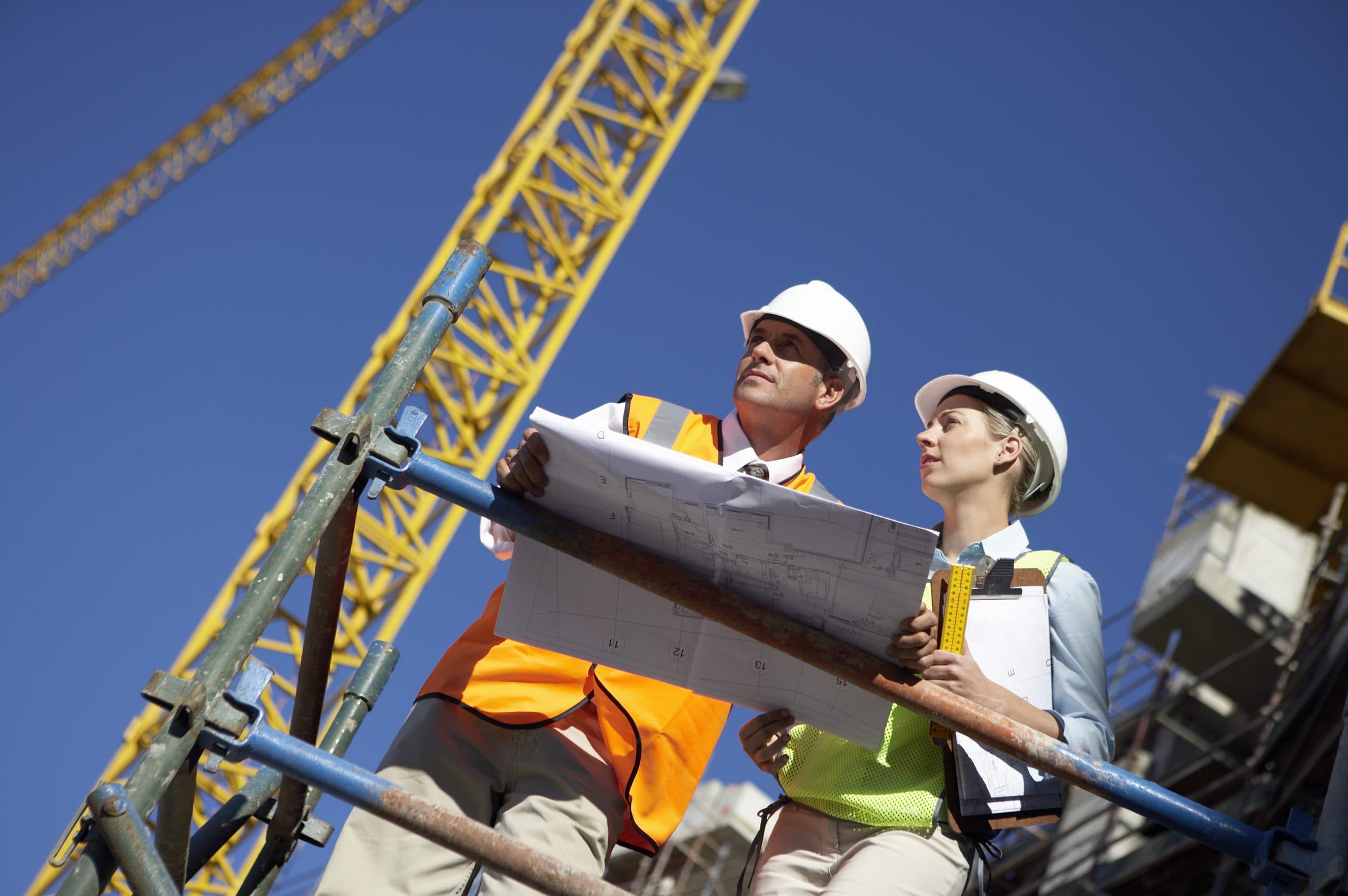 Construction workers reviewing plans on a platform beside a crane